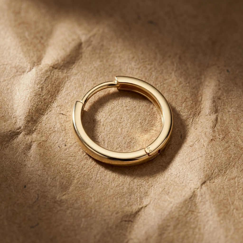 Overhead view of a 20mm gold hoop earring on textured kraft paper, showcasing shine and micro-polished details with cinematic lighting.